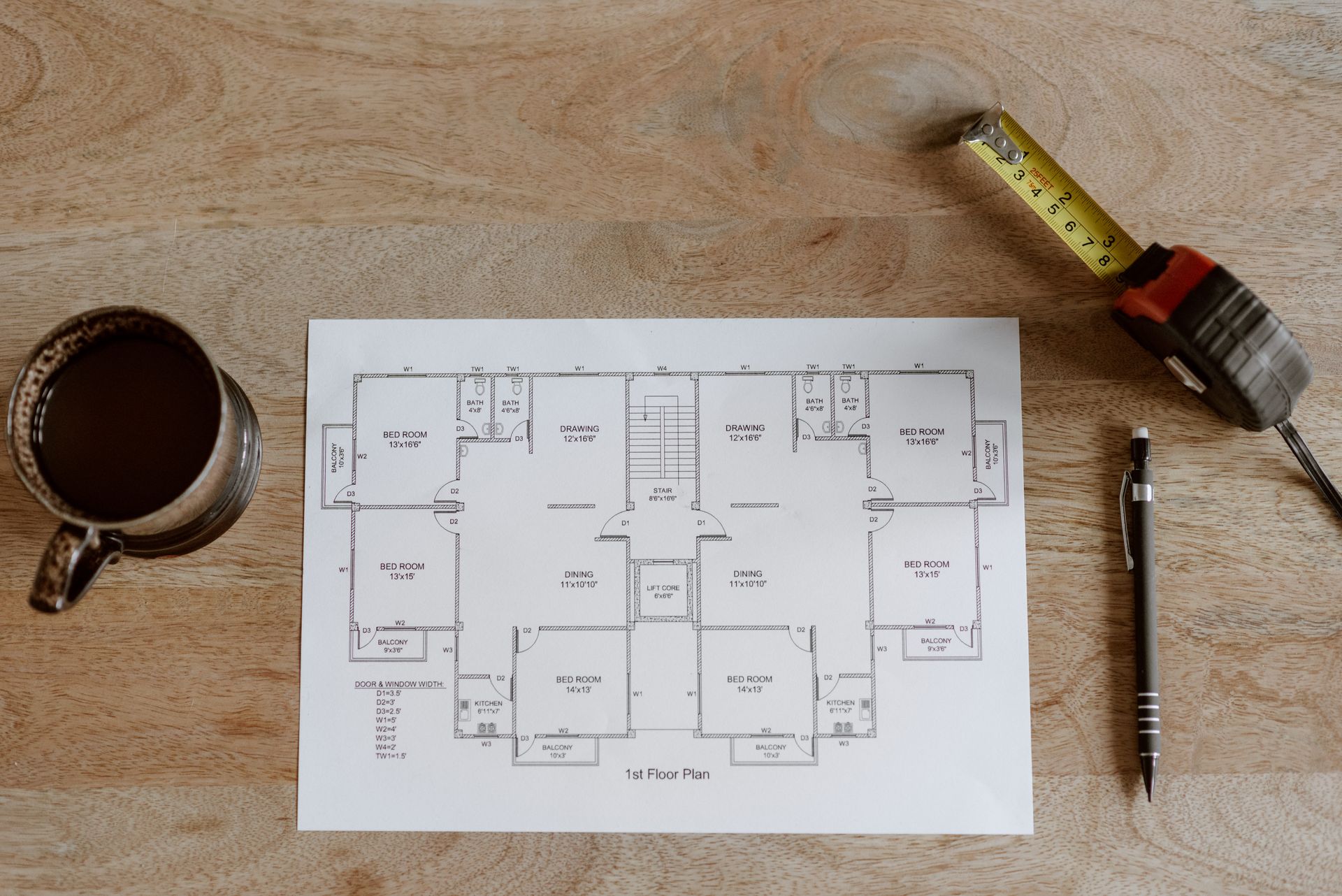 A floor plan, measuring tape and pen on a desk